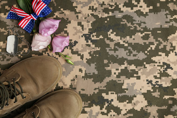 Flat lay composition with military boots and flowers on camouflage background, space for text. Armed Forces Day