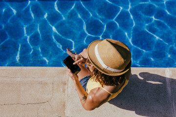 young woman using mobile phone at the swimming pool. Summertime, technology and lifestyle outdoors