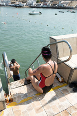 Young swimmer woman who has no arms or legs entering the sea with the competition number painted on her back.