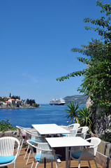 close-up of white tables and chairs on the terrace overlooking the blue Adriatic sea on which the cruise ship sails.