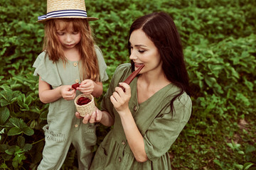 Fototapeta premium Beautiful young mother with her daughter having fun on a green field with strawberries