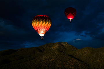 Colorful glowing hot air balloons floating in a night sky over forested mountain peaks
