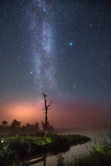 Fishermen boats docked at a still lake with sunset in the background. Glowing milky way over the landscape. Tropical summer nights with million stars above and colorful sky. 