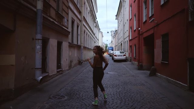 Young beautiful girl turns around and runs on a European street. A smiling cheerful woman looks back.