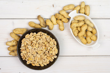 Lot of whole lot of halves of natural yellow peanut in white oval ceramic bowl in dark ceramic bowl flatlay on white wood