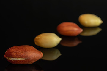 Group of four whole natural yellow peanut placed diagonally in line isolated on black glass