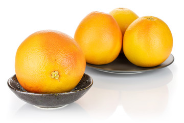 Group of four whole fresh pink grapefruit in dark ceramic bowl on gray ceramic plate isolated on white background