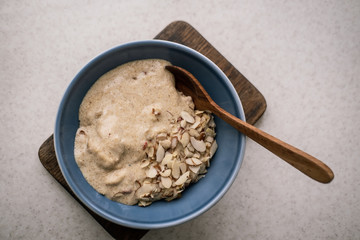 Flaxseed porridge with almonds and coconut milk in a blue bowl, wooden spoon on white marble table