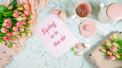 Welcoming Spring theme concept flat lay tea break with pink roses and female accessories on white marbel background.