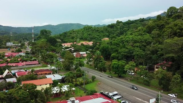 Aerial, rising, drone shot, overlooking traffic, in a small town, in middle of the rainforest at Barrio Las Parcelas, on a cloudy, summer day, in Costa Rica