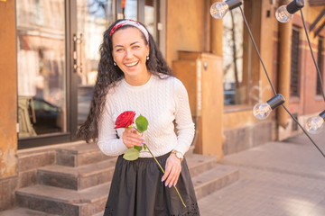 Fototapeta premium Young beautiful pretty girl with long hair with red rose in the city