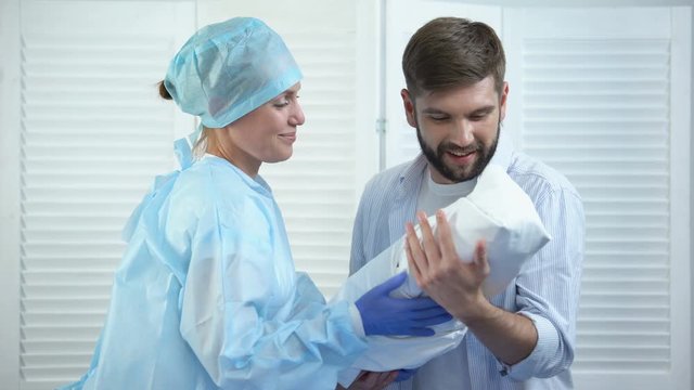 Smiling nurse giving young happy father newborn child, miracle of birth, care