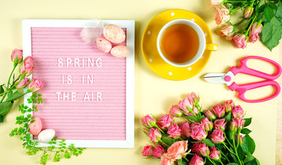 Welcoming Spring pink and yellow theme concept flat lay tea break with roses and gardening accessories.