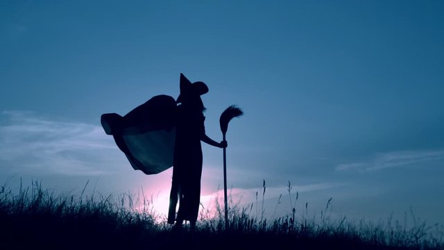 woman in a witch costume and broom have fun slow motion view on evening blue sky halloween holiday