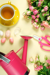 Welcoming Spring pink and yellow theme concept flat lay tea break with roses and gardening accessories.