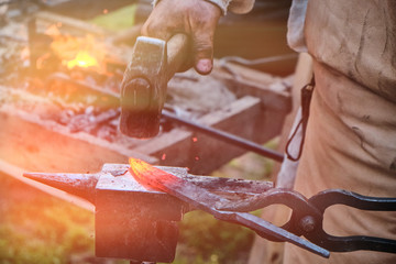 The blacksmith has a hammer on hot iron. The workpiece is clamped in the grip of the master....