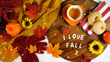 Autumn Fall theme flatlay overhead with cosy sweater, bagels, cups of herbal tea and scattered maple leaves.