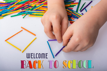 Kid making geometric shapes with colorful sticks on white background