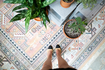 Woman’s perspective of her shoes, plants on floor, vintage pink rug