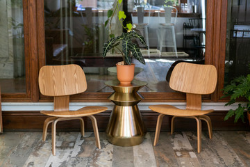 house plant in terra cotta vase on gold side table between two wooden chairs, mid century modern home decor