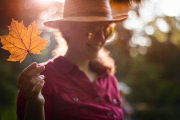 Happy Young Woman in a Red Shirt Smiling Holding a Maple Leaf in Autumn