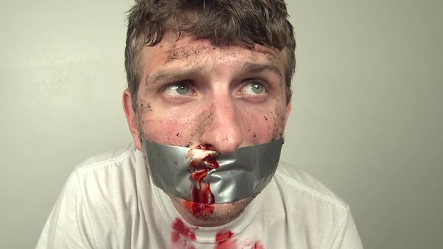 Man with bloody face breathing hard, while duct tape is on face.
