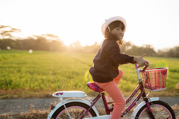 happy kid girl riding her bicycle outdoor during sunset