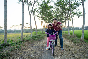 supportive asian dad help her kid to ride bicycle outdoor