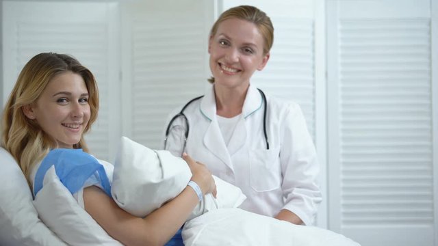 Doctor and mother holding newborn child smiling at camera, skin-to-skin contact