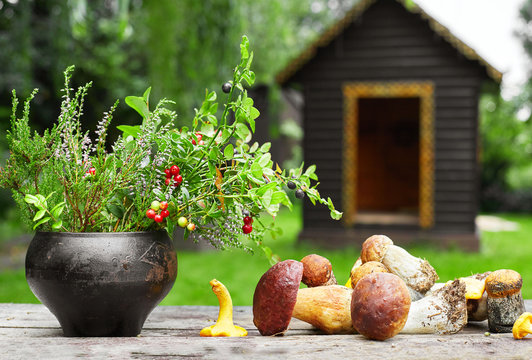 Wild mushroom and bouket of wid berry in the old iron pot and nice wooden house on the back