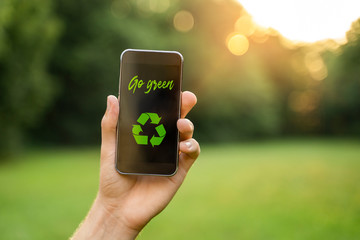 Go green concept, man in nature holding smartphone with go green text and recycle symbol 