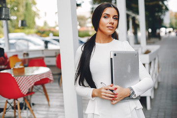 Beautiful girl with a laptop. Woman in a summer city. Lady in a white blouse