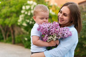Young loving mother walking with her little son on spring background. Cute child and her mom on outdoor. Enjoy the good weather and spring flowers. Happiness to be a parent. Time together. 