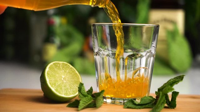 Orange soda slow motion fill glass with ice. Fanta soda drink. Glass stand on wooden plate with lime and mint on it.