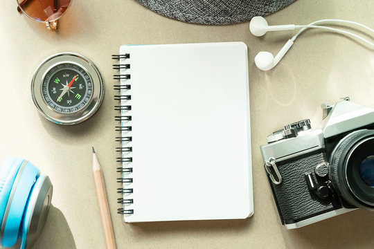 Empty opened white page of notebook with pencil, camera, compass and accessories on table. Travel background concept.