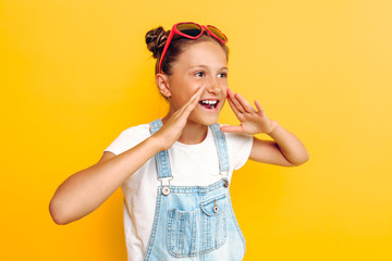 Portrait of a happy teenager, girl screaming good news at camera, standing on yellow background