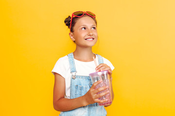 Happy teenager dreams looking at empty space on a yellow background with a refreshing drink in her hands
