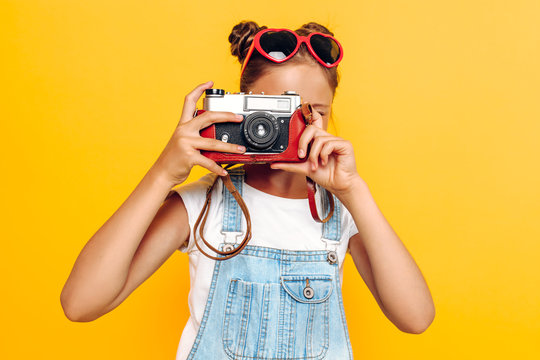 Stylish young girl, a teenager holds a camera in his hands and takes pictures on a yellow background