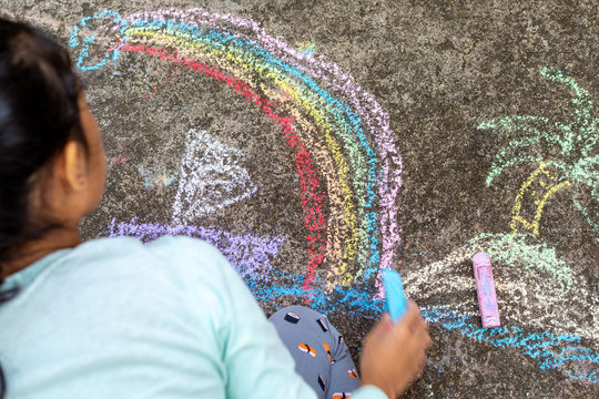Girl drawing with colorful chalk crayons on  concrete
