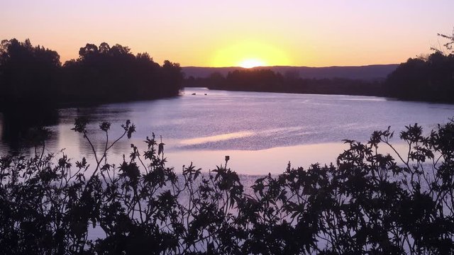 The sun sets over the Hawkesbury River at Windsor, west of Sydney, Australia. In the distance two fishing boats and the Blue Mountains.