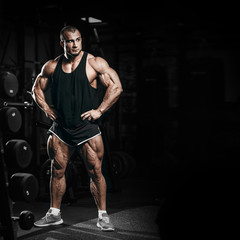 Fototapeta na wymiar Muscular athletic bodybuilder man in gym over dark background with dramatic light posing and resting after hard training work out. Sport bodybuilding photo concept with copy space