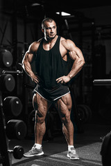 Fototapeta na wymiar Muscular athletic bodybuilder man in gym over dark background with dramatic light posing and resting after hard training work out