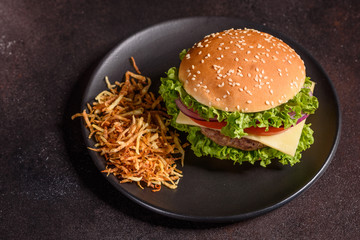 Tasty grilled homemade burger with beef, tomato, cheese, cucumber and lettuce. Delicious grilled burgers. Craft beef burger and french fries on wooden table.