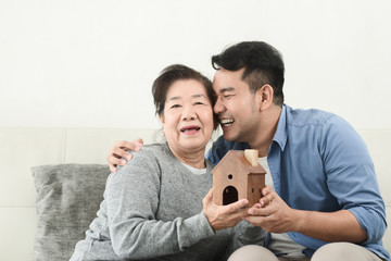 Asian man buy house for his mother, real estate concept.  Mother kissing her son for love.