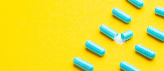 Blue tablets in capsules. One capsule is open. Yellow background. Copy space for text.