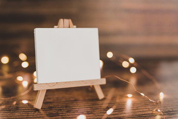 black canvas miniature surrounded by fairy lights on wooden desk with copyspace