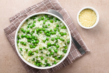 Fresh homemade creamy green pea risotto in bowl, spoon and grated cheese on the side, photographed overhead