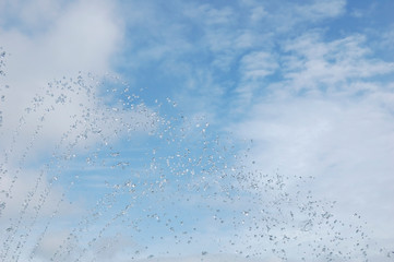 Splashes and drops of water, pleasantly formed by a fountain. on the background, the blue sky with white clouds.