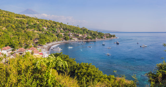 Aerial view of Amed beach in Bali, Indonesia. Traditional fishing boats called jukung on the black sand beach and Mount Agung volcano in the background, partially covered by clouds