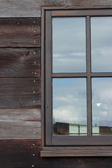 large window on a wooden building reflecting the sky on a cloudy overcast day